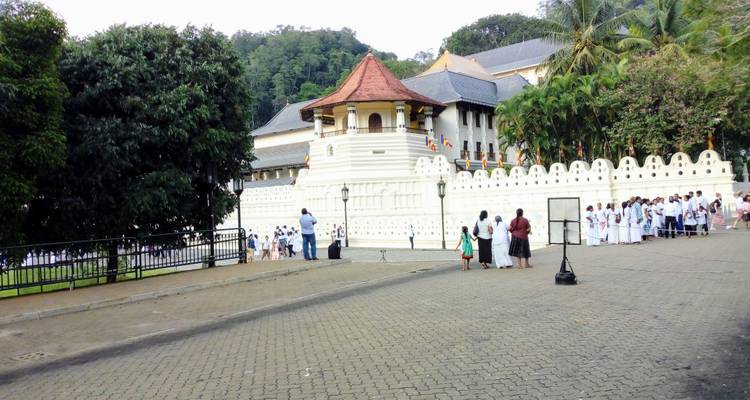 Les habitants vêtus de blanc se rassemblent à l'extérieur du complexe du Temple de la Dent avec ses murs blancs richement ornementés à Kandy.