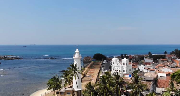 Une vue aérienne du phare du Fort de Galle, des palmiers et de l'océan Indien turquoise rencontrant les anciens murs de la ville.