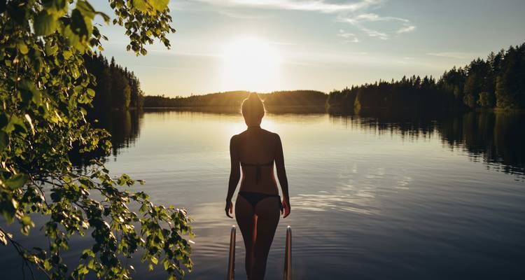 Persoon in zwemkleding die een meer bij zonsondergang onder ogen ziet.