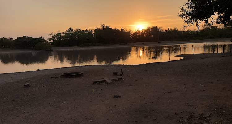Een warm oranje zonsondergang weerspiegeld in een rustige bocht van de rivier, omlijst door silhouetachtige bomen.