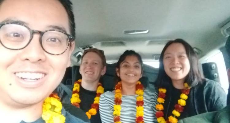 Cuatro viajeros sonrientes usando guirnaldas de caléndula dentro de un auto tomándose una selfie.