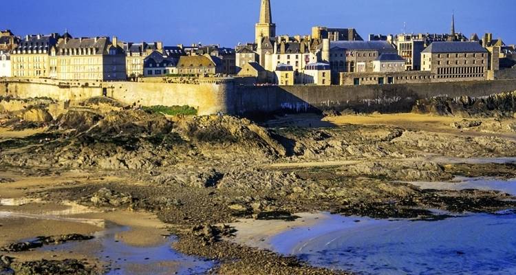 Ommuurde kuststad met rotsachtige stranden onder een blauwe hemel.
