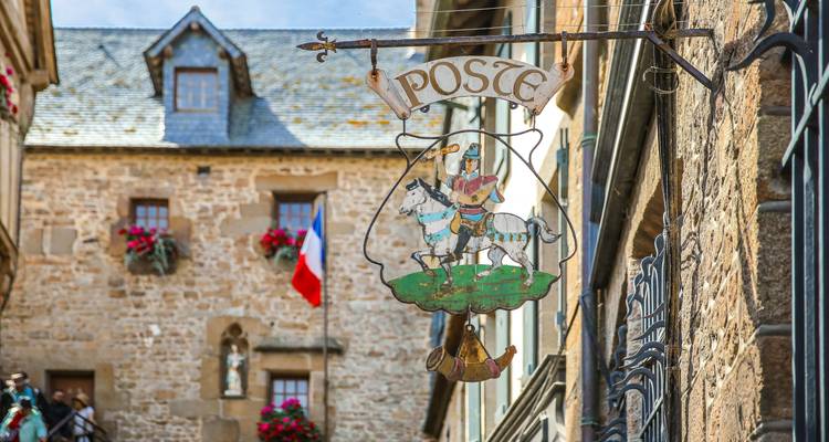 Cartel decorativo vintage de Correos cuelga sobre una calle de piedra con bandera francesa en Mont Saint-Michel