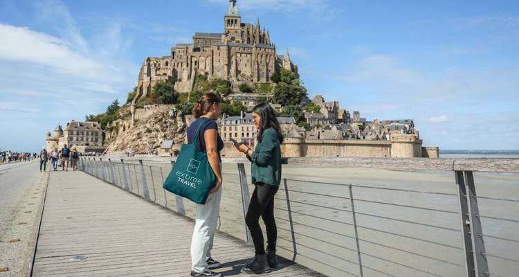 Guide et voyageur s'arrêtent pour converser sur la passerelle menant au Mont-Saint-Michel avec les vasières visibles