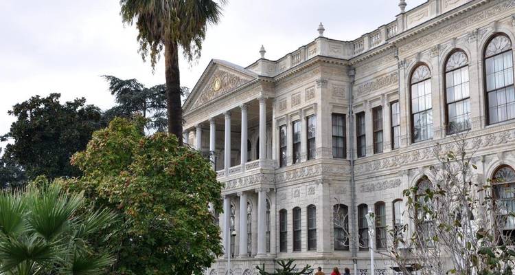 Edificio histórico ornamentado con columnas y árboles en primer plano.