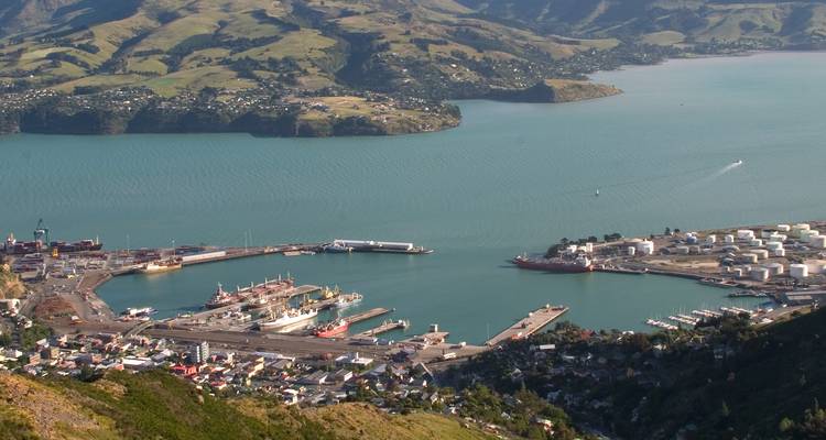 Point de vue élevé surplombant une baie aux contours verdoyants et un port actif avec des quais et des navires encadrés par des collines ondulantes.