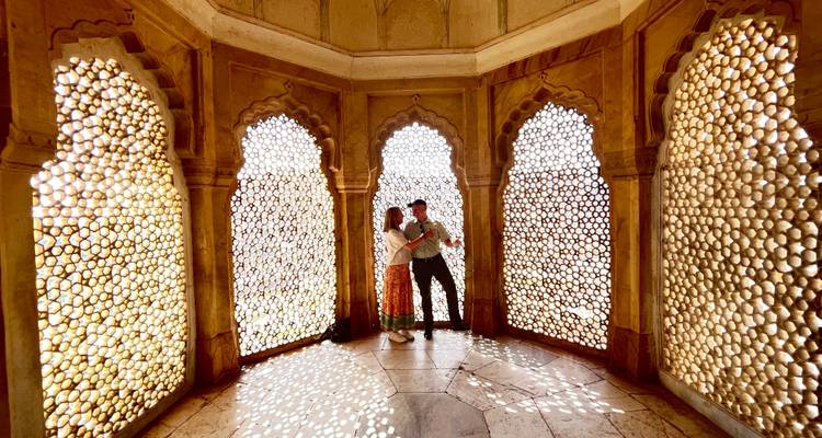 Dos personas de pie dentro de una estructura arquitectónica decorativa con ventanas enrejadas.