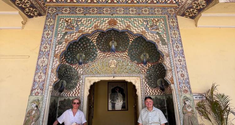 Dos personas posando bajo una entrada con tema de pavo real.