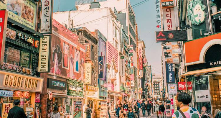 Calle de compras vibrante llena de señales de tiendas coloridas y multitudes de peatones.