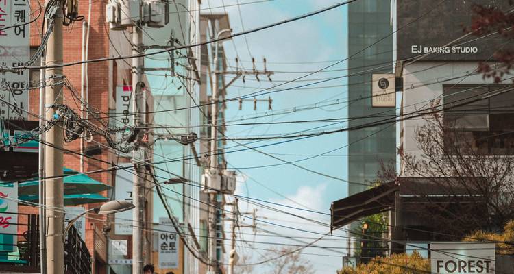 Una calle de una ciudad coreana entrecruzada por cables de electricidad y salpicada de letreros de tiendas bajo un cielo azul.
