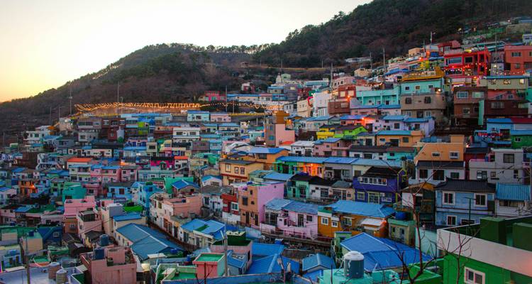 Las casas de colores vibrantes de la aldea cultural de Gamcheon brillan con la luz del atardecer bajo una cresta boscosa.