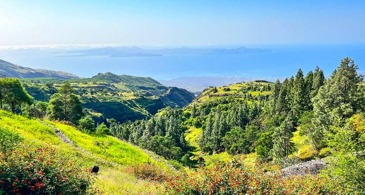 Valle exuberante y verde descendiendo hacia un océano azul con islas distantes bajo cielos despejados