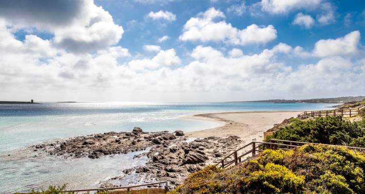 Plage vaste et littoral rocheux avec une eau azur étincelante sous des nuages épars près de Stintino.