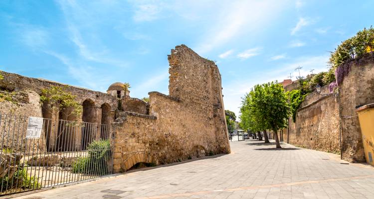 Vestiges d'un ancien mur en pierre et d'une porte le long d'une rue pavée tranquille bordée d'arbres à Cagliari.
