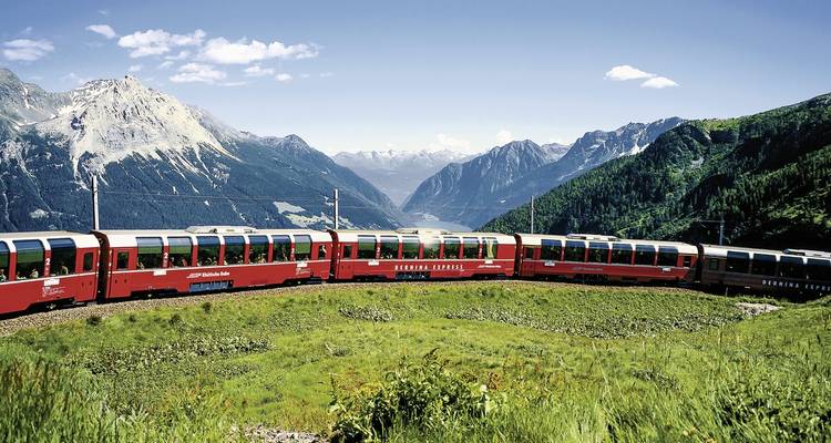 Bernina Express train winding through green pastures and mountains.