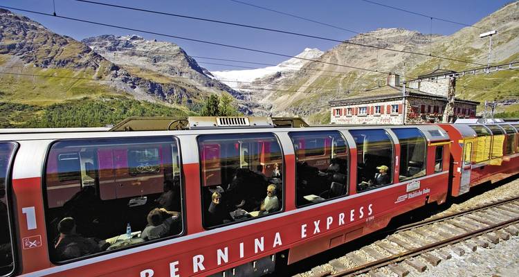 Tourist train passing through a rugged mountain landscape.
