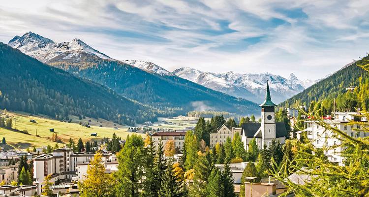 Alpine town framed by snow-dusted peaks, evergreen forests and a picturesque church spire.