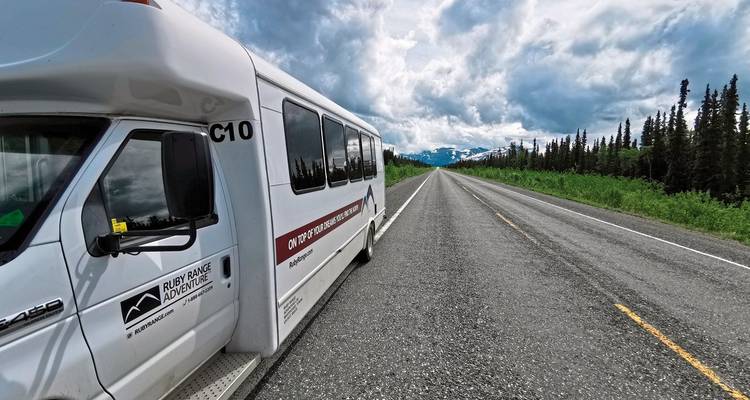 Ein Tourbus, der auf einer langen offenen Straße mit Bergkulisse geparkt ist.
