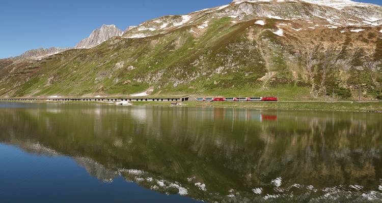 A scenic train journey through mountainous terrain with a reflective lake.