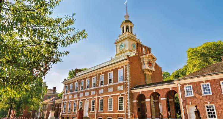 Red-brick Independence Hall with tall clock tower framed by leafy trees against a clear sky.