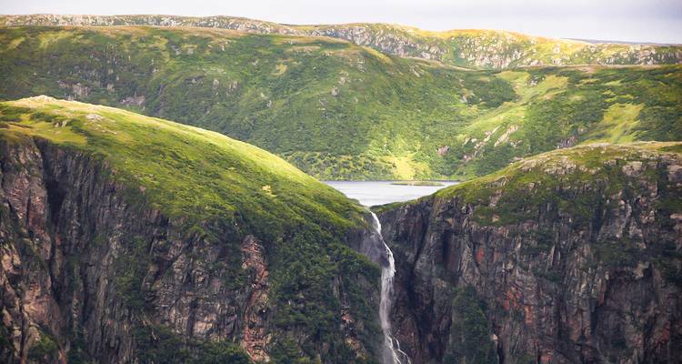 Tiefe Flussschlucht mit einem langen Wasserfall, der zwischen steilen grünen Felswänden in Neufundland hinabstürzt