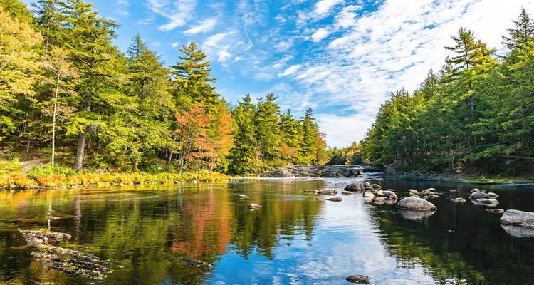 Rivière forestière tranquille reflétant des arbres aux teintes automnales sous un ciel nuageux lumineux et dégagé