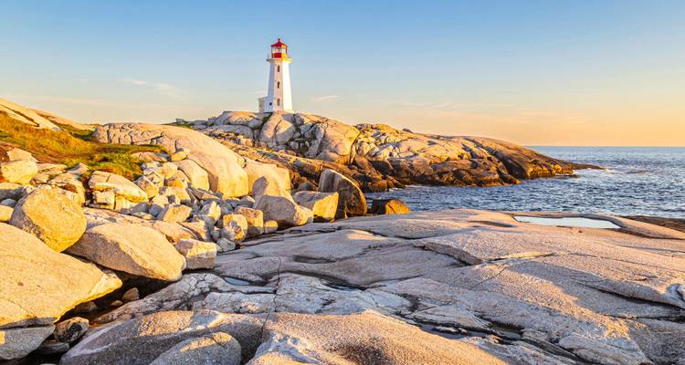 Phare blanc emblématique perché sur des rochers de granit illuminés par le soleil à Peggy's Cove pendant l'heure dorée