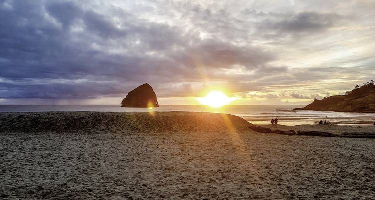 Plage de sable au coucher du soleil avec une formation rocheuse proéminente en silhouette.