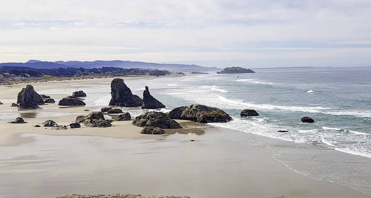 Sandiger Strand mit verstreuten Felsen und Meereswellen.