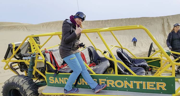Person posiert mit einem Strandbuggy in einem sandigen Bereich.