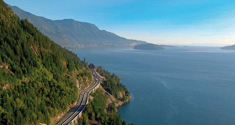 Kusthoofdweg die zich langs de oceaan uitstrekt met beboste heuvels.