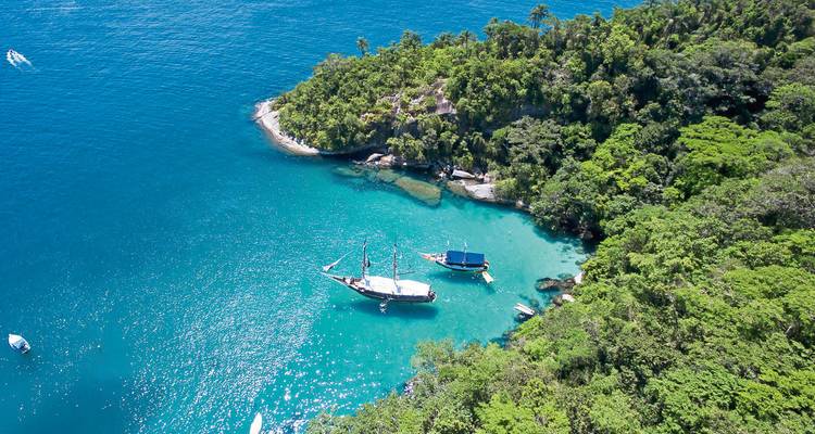 Vue aérienne de voiliers dans une crique turquoise entourée d'une forêt tropicale luxuriante.