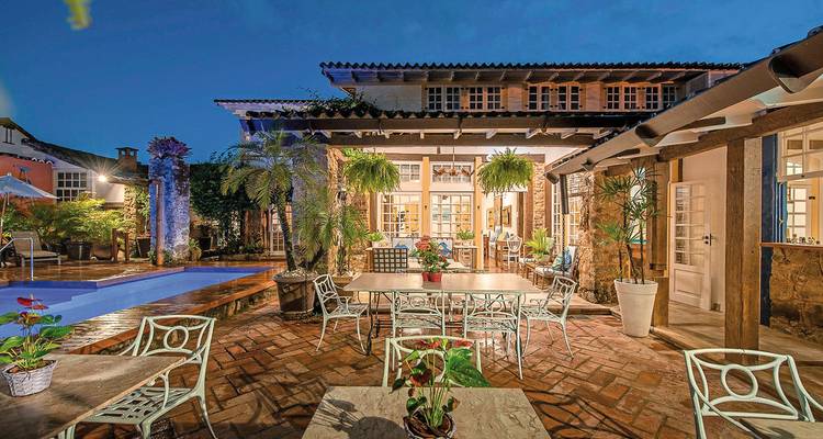 Espace de restauration extérieur au bord d'une piscine, entouré de plantes luxuriantes et d'un bâtiment charmant.