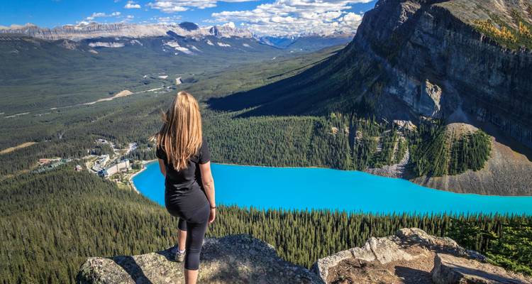 Frau, die auf einer Klippe steht und auf einen leuchtend blauen See blickt.
