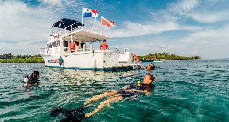 Des gens nagent et font de la plongée avec tuba près d'un bateau dans des eaux turquoise claires.