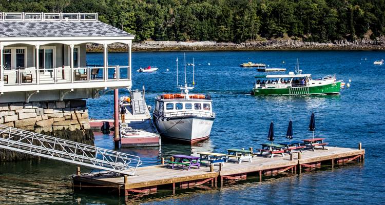 Here's the German translation:
Boote, die neben einem Küstengebäude mit Bäumen im Hintergrund angelegt haben.
Alternative translation:
Boote liegen an einem Küstengebäude vor Bäumen im Hintergrund.