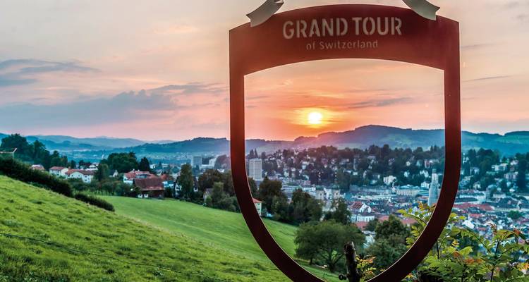 Scenic overlook of a town at sunset with Grand Tour sign.