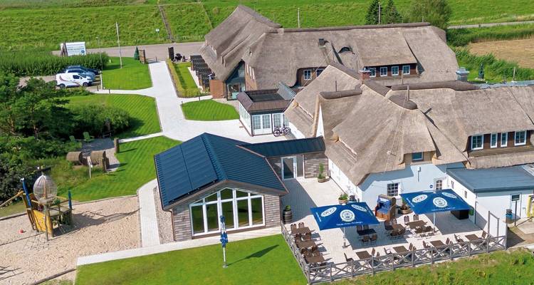 Luftaufnahme eines Resorts mit reetgedeckten Gebäuden und grünen Rasenflächen.