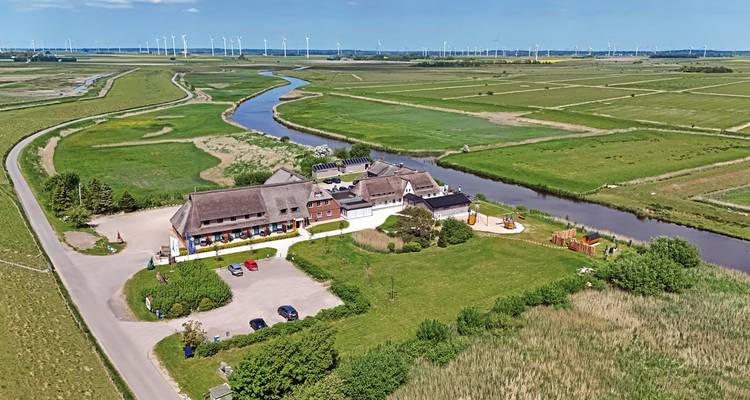 Luftaufnahme einer Landschaft mit einem Hotel, Fluss und Windrädern in der Ferne.