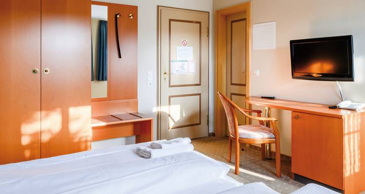 Hotelzimmer-Interieur mit Bett, Fernseher und Schreibtisch.