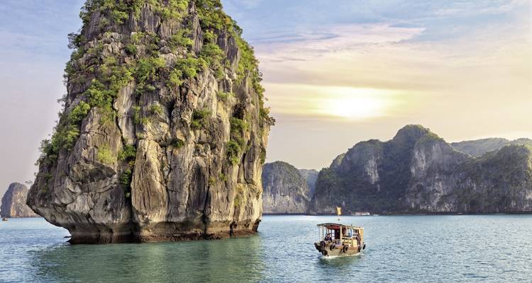 Sunset view of Halong Bay with a boat and rock formations.