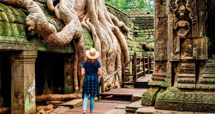 Un voyageur explorant le temple Ta Prohm avec de grandes racines sur les pierres.