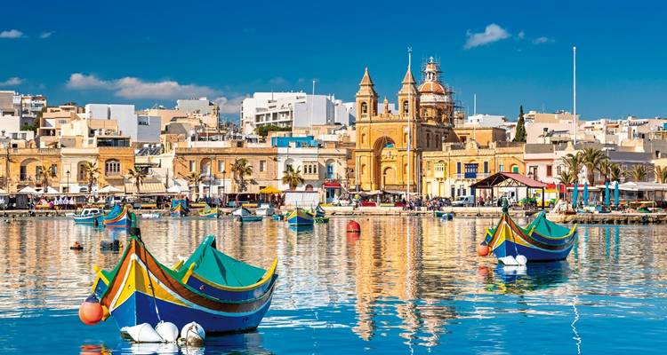 Harbor with traditional Maltese boats and a city in the background
