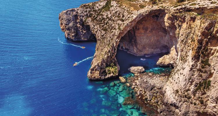 Rocky cliff and azure blue water with small boats passing by
