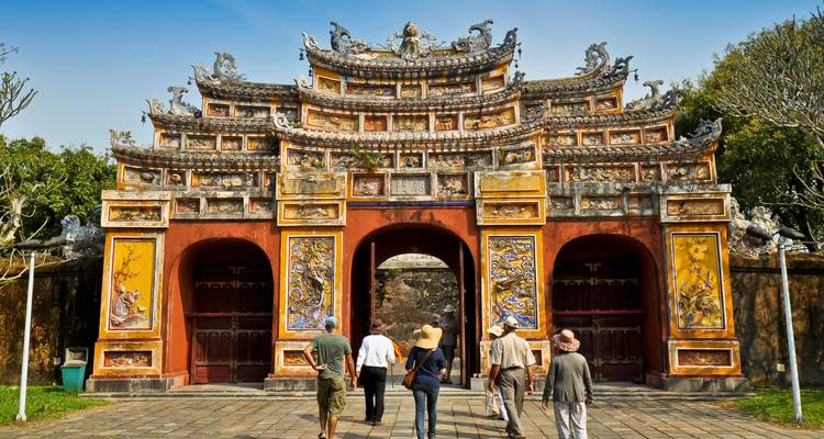 Des gens marchant vers une porte historique vietnamienne aux motifs complexes.