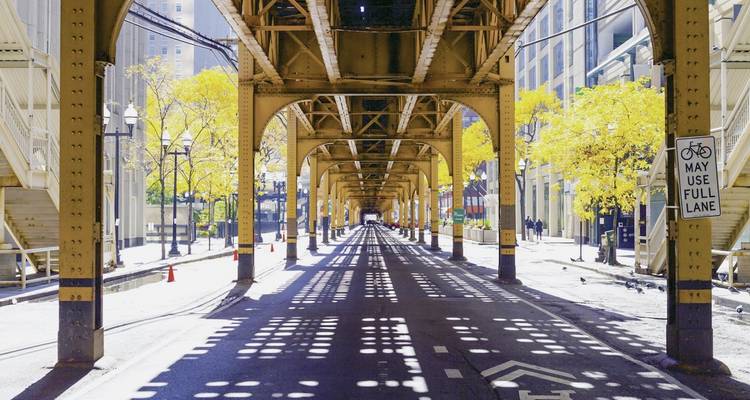 View of an urban scene under elevated train tracks with shadows.