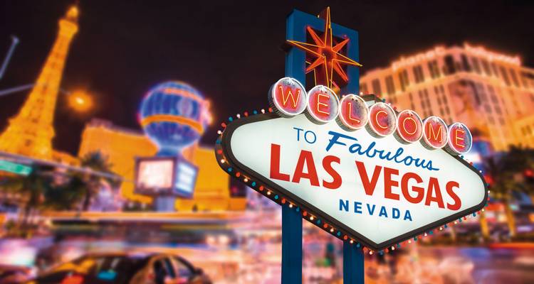 Ikonisches beleuchtetes "Welcome to Fabulous Las Vegas" Schild mit unscharfem Nachtleben im Hintergrund.