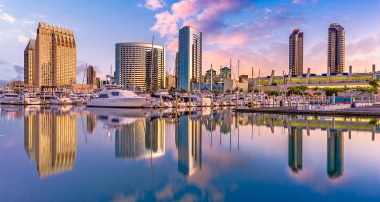 Horizonte de San Diego con edificios y puerto deportivo al atardecer, reflejándose en aguas tranquilas.