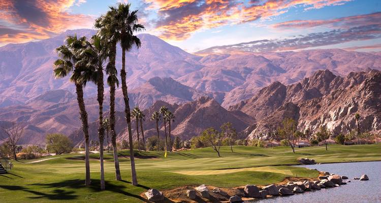 Palmeras junto a un campo de golf con montañas de fondo al atardecer.