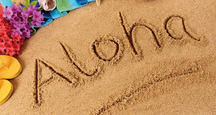 La palabra "Aloha" grabada en la arena de la playa cerca de artículos tropicales coloridos.